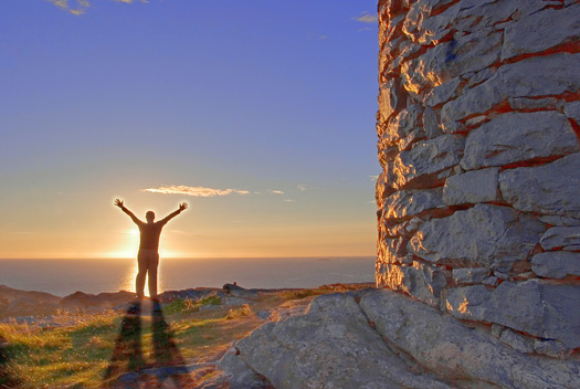 A silhouetted man in front of the sun stretching arms and and glowing. Atlantic Ocean