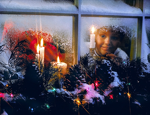 A child's expectant face seen through a frosted window with Christmas candles