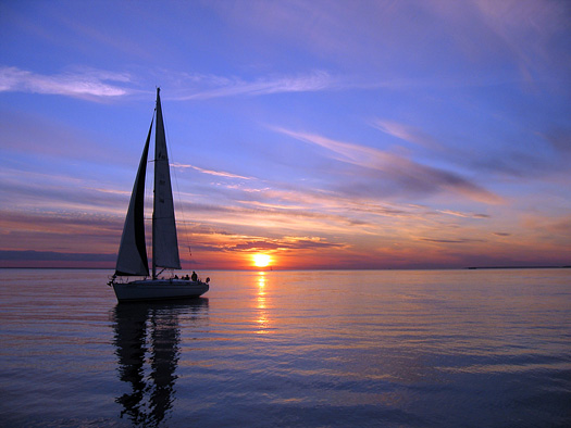 Single sailboat silhouetted against sunset