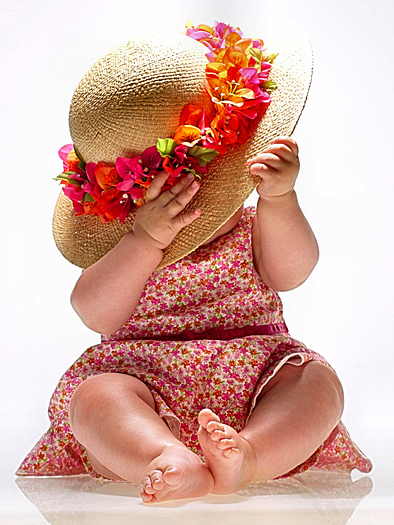 Seated baby in pink-flowered dress with straw hat over her face