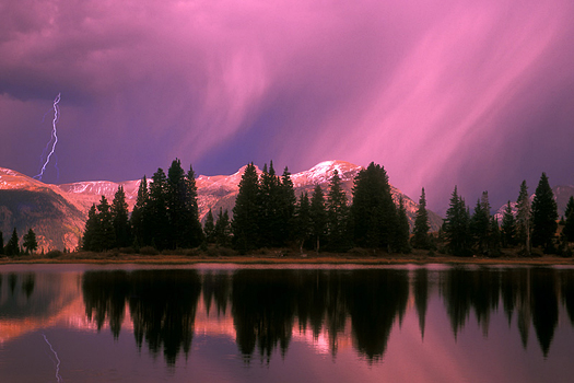 A reflecting mountain lake with a pink and purple sky after a storm