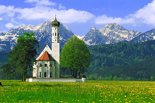 Russian church in a field with yellow flowers. Mountains in the background.