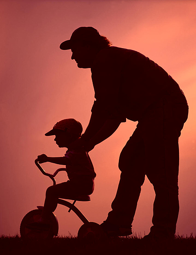 Silhouette of father teaching child to ride bike
