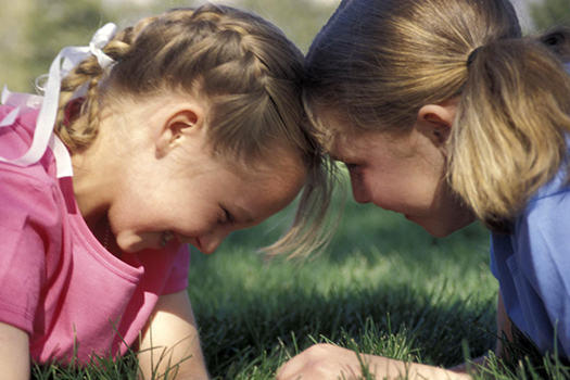 Two little girls with their heads together playing together outside