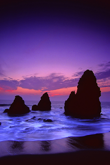 Ocean sunset with three large, craggy rocks at the shoreline