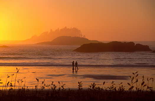 Two people walking on a beach during a sunset in Tofino, British Columbia.