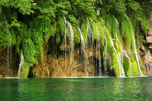 Waterfall over mossy stones and green pool